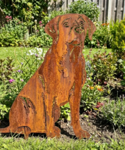 Metalen labrador retriever silhouet met natuurlijke roestpatina in een groene tuinborder