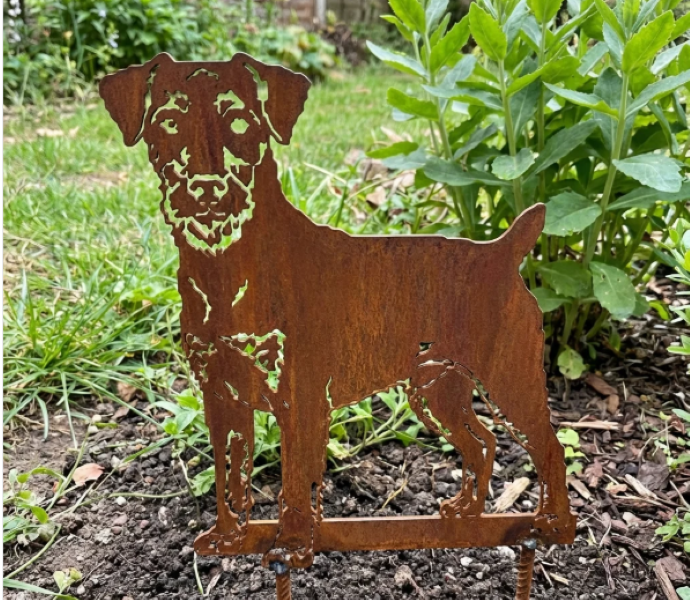 Metalen Duitse Jachtterriër silhouet met natuurlijke roestlaag tussen planten in de border